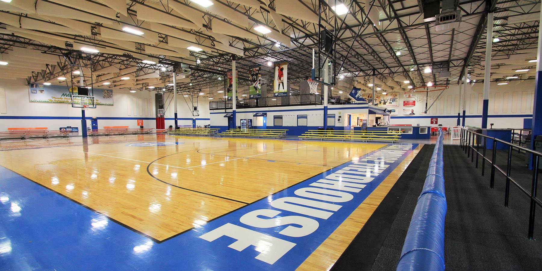 Indoor basketball court with bright lights overhead. The course has a blue painted boarder on the floor
